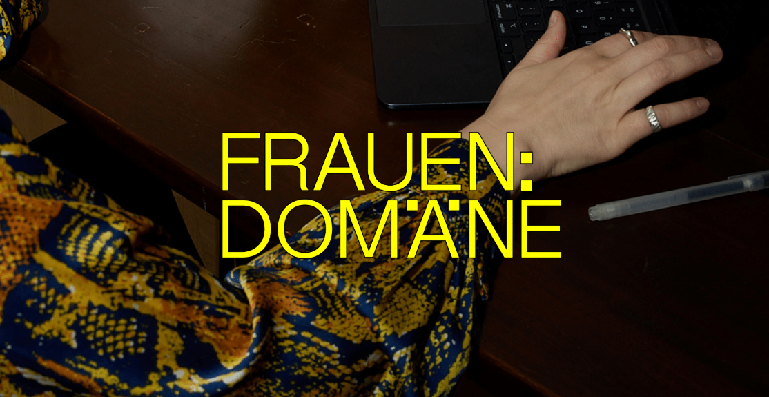 Gelber Schriftzug „FRAUEN:DOMÄNE“ über dunklem Hintergrund und der Hand einer Frau. Sie trägt eine Bluse mit gelb-blauem Schlangenmuster.